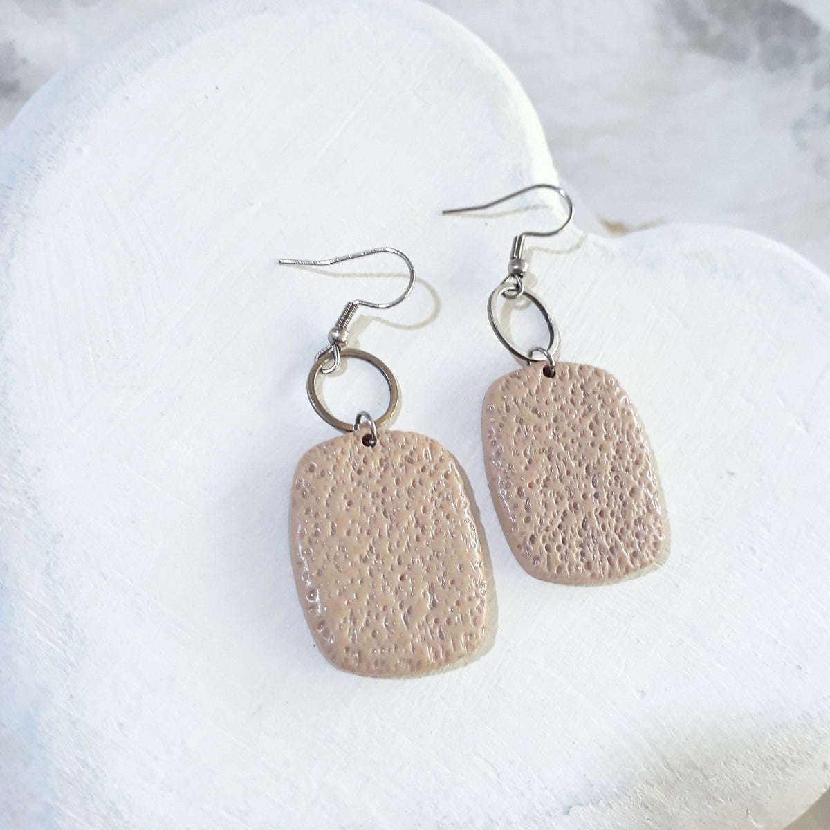 Warm beige polymer clay rounded rectangle earrings with a stippled texture, open silver-tone circular connectors and shepherd hooks.