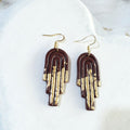 Glossy dark-brown polymer clay stepped arch earrings with gold-coloured accents across the lower curves and gold-tone ear hooks.