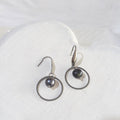 Dark charcoal near-round freshwater pearls suspended inside open silver-tone circles on elegant stainless steel ear hooks.