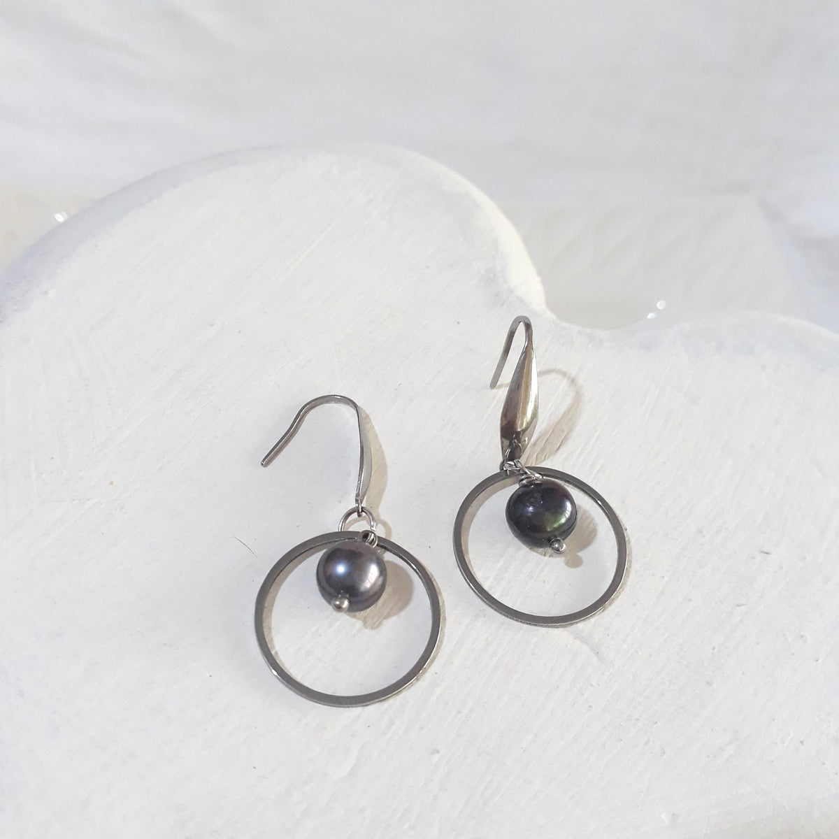 Dark charcoal near-round freshwater pearls suspended inside open silver-tone circles on elegant stainless steel ear hooks.