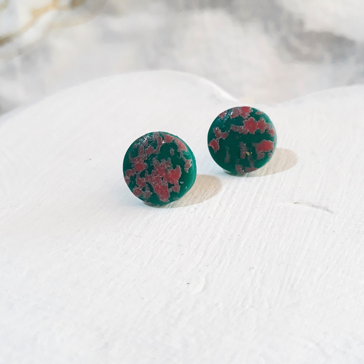 Dark jade-green round polymer clay stud earrings with scattered pink inlays and glossy surfaces.