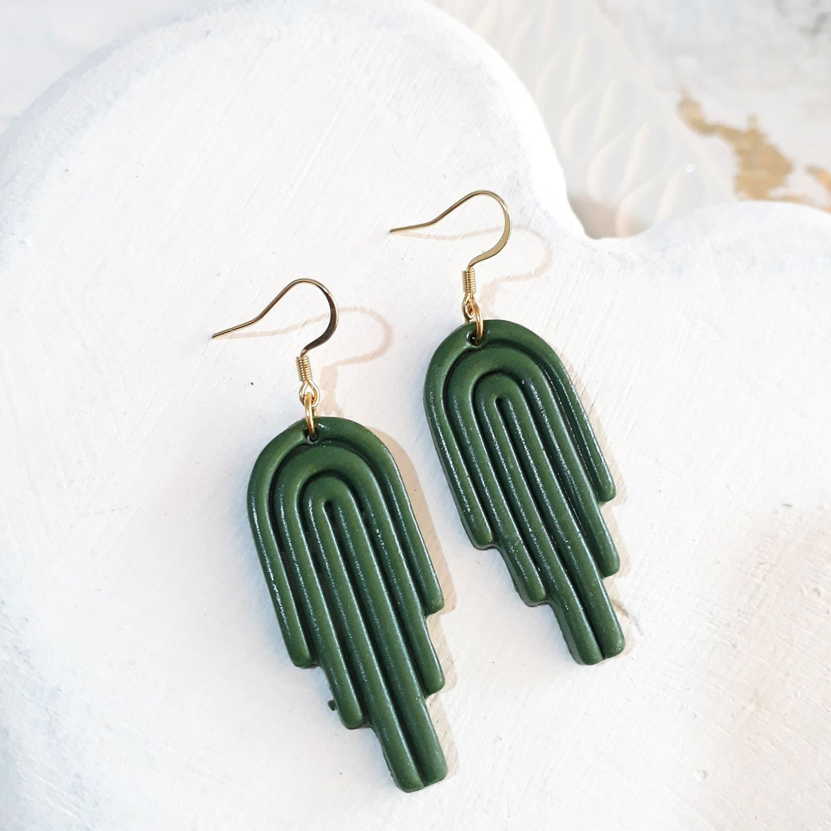 Deep green glossy polymer clay stepped arch earrings with curved line detailing and gold-tone shepherd ear hooks.
