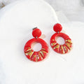 Deep-orange polymer clay earrings with round stud tops and open circular drops decorated with radiating grooves and gold-coloured accents.