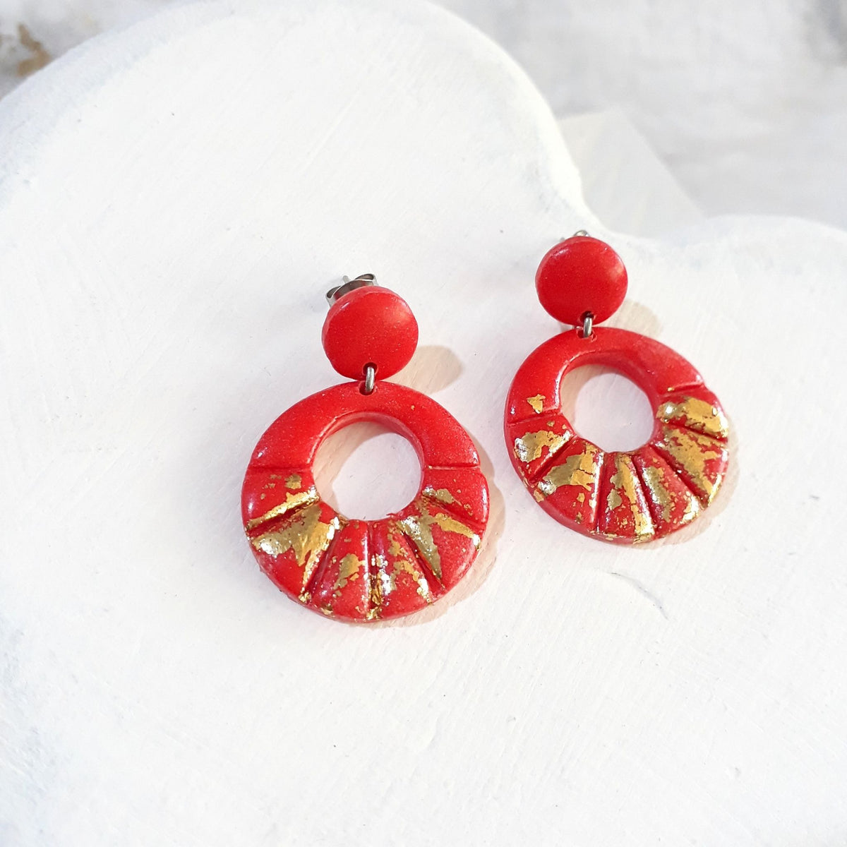 Deep-orange polymer clay earrings with round stud tops and open circular drops decorated with radiating grooves and gold-coloured accents.