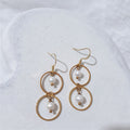 Gold-plated stainless steel double circle dangle earrings with a white freshwater pearl suspended inside each circle and shepherd hooks.