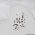 Stainless steel double circle dangle earrings with a white freshwater pearl suspended inside each circle and shepherd hooks.