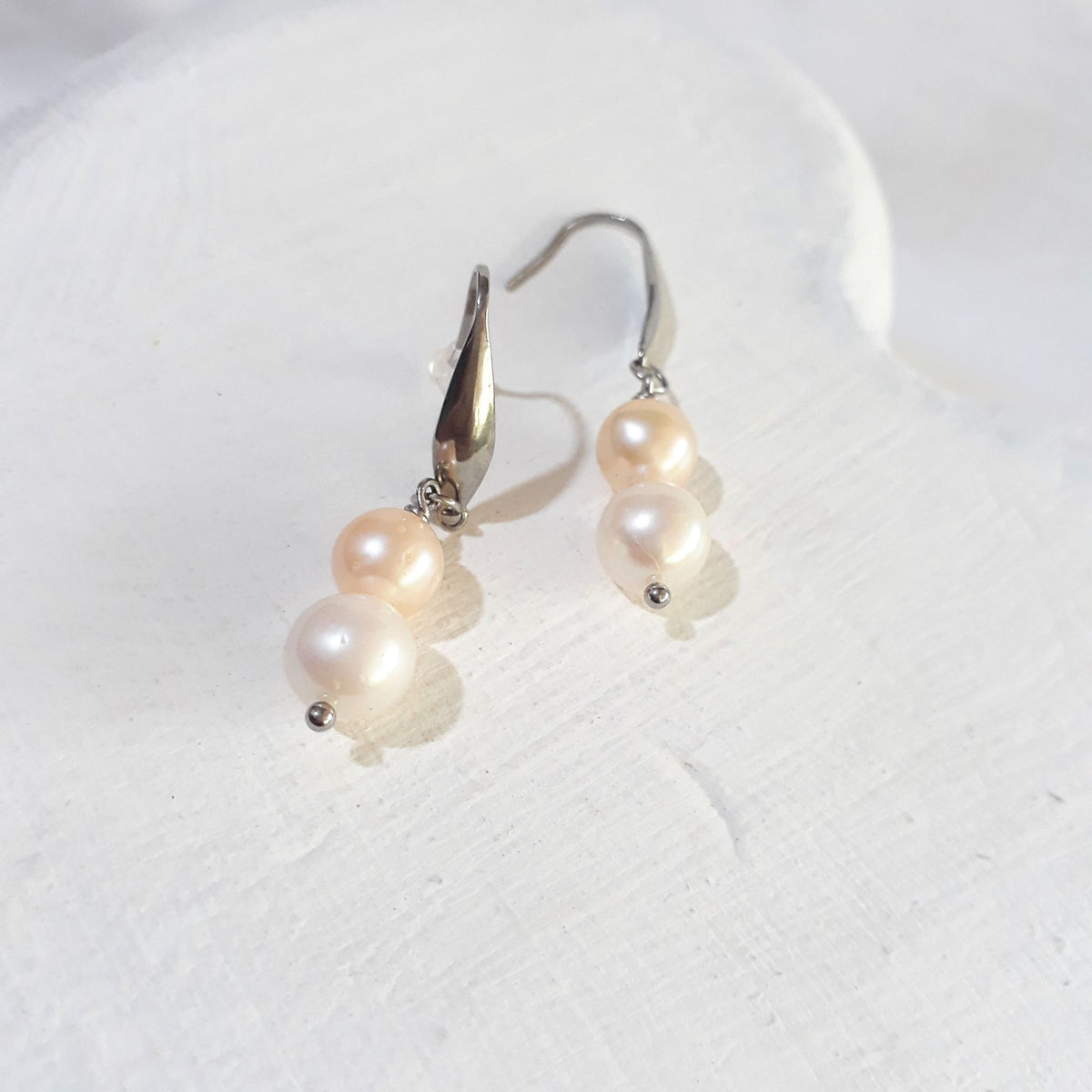 Double freshwater pearl drop earrings with peach-pink pearls above white pearls on silver-tone elegant ear hooks.
