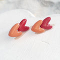 Glossy polymer clay stud earrings with overlapping salmon-pink and dark-pink hearts.