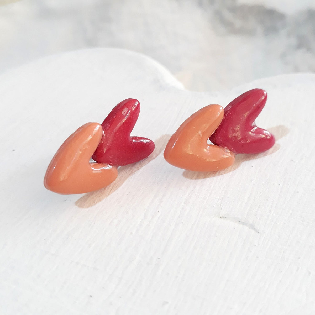 Glossy polymer clay stud earrings with overlapping salmon-pink and dark-pink hearts.