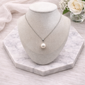 Pearl necklace on a white bust with a marble base and flowers in the background