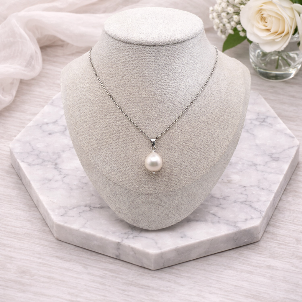 Pearl necklace on a white bust with a marble base and flowers in the background