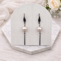 Pearl earrings on a white marble stand with flowers in the background