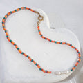 This handmade necklace pairs white freshwater pearls with small orange, red and green glass beads, bringing little bursts of colour to their soft lustre