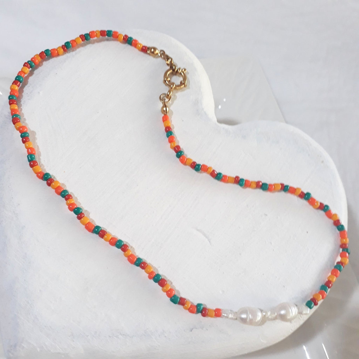 This handmade necklace pairs white freshwater pearls with small orange, red and green glass beads, bringing little bursts of colour to their soft lustre