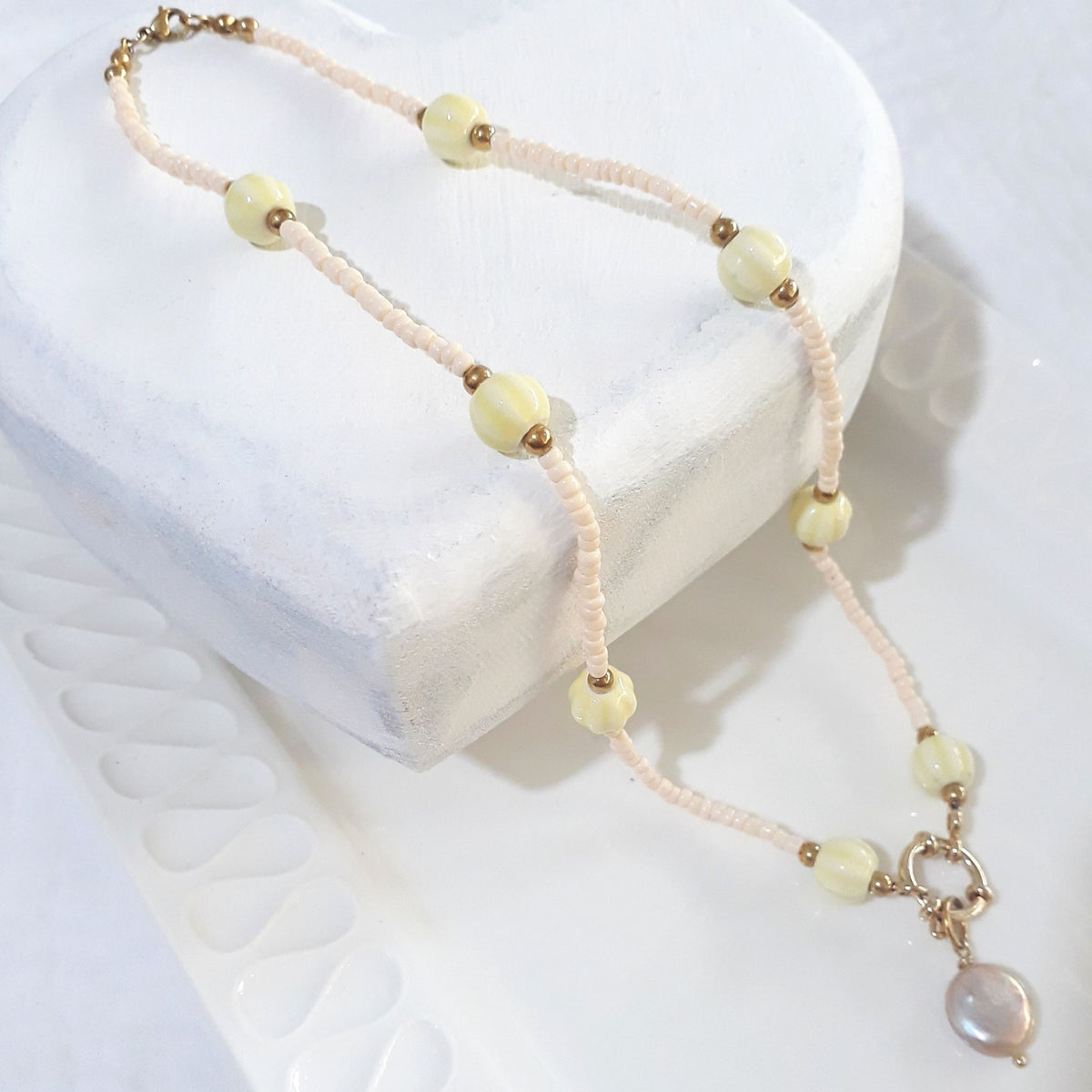 This handmade necklace pairs a peach-pink freshwater coin pearl with small beige glass beads and eight soft yellow ceramic beads