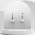 Pearl earrings on a white pedestal with a light gray background