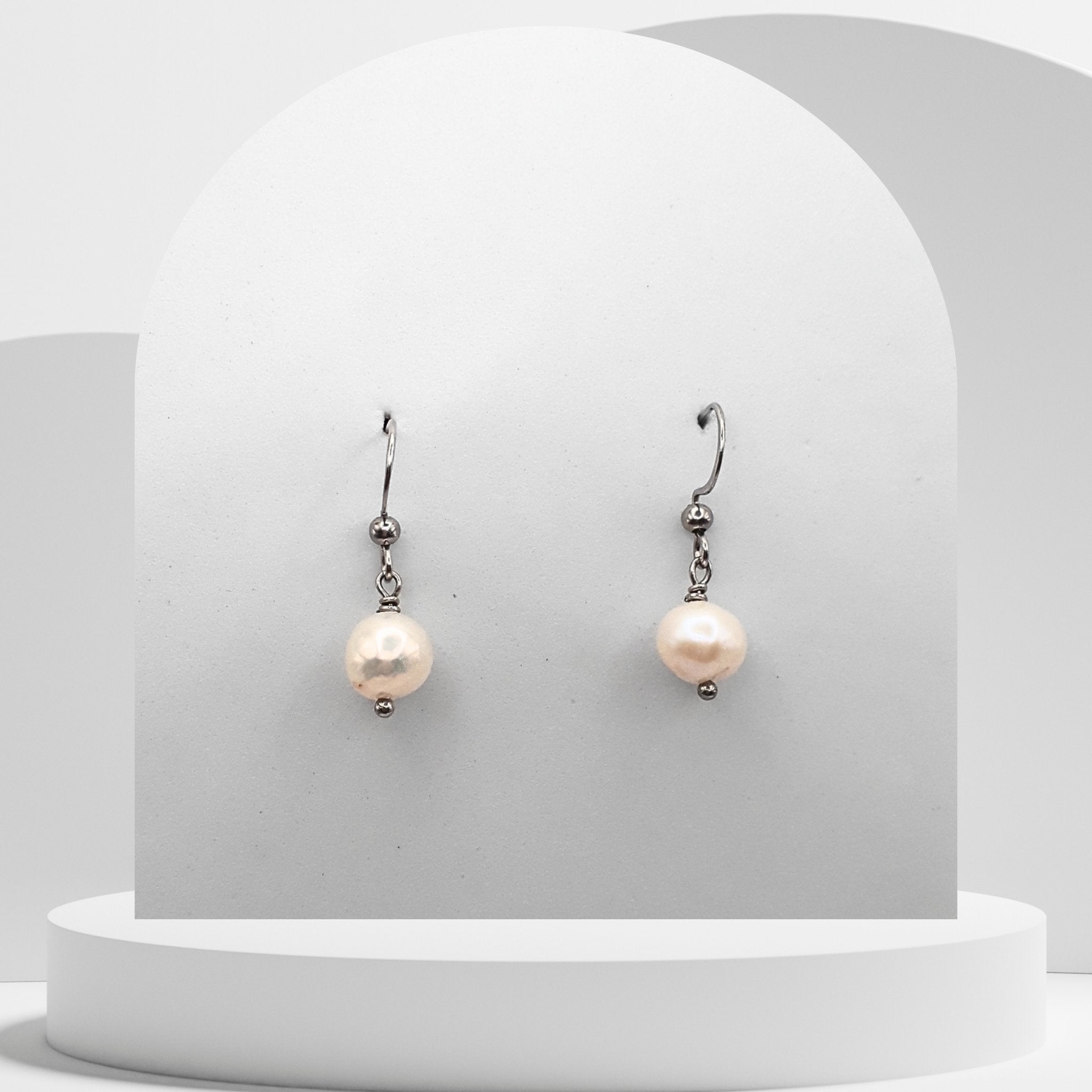 Pearl earrings on a white pedestal with a light gray background