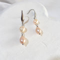 Peach-pink freshwater pearl dangle earrings with teardrop pearls linked beneath smaller irregular pearls on silver-tone elegant ear hooks.
