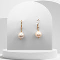 Pearl earrings with gold hooks on a white pedestal