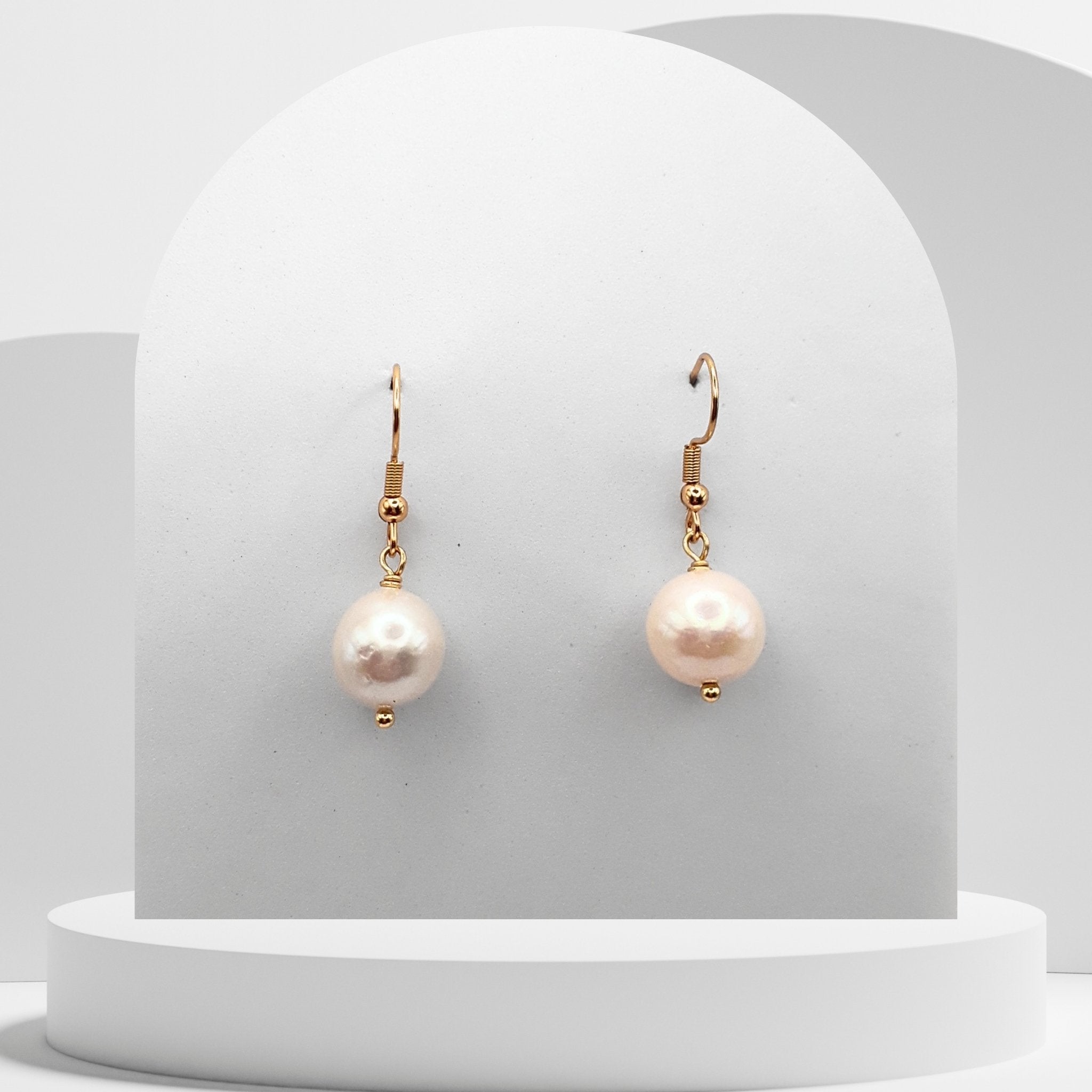 Pearl earrings with gold hooks on a white pedestal
