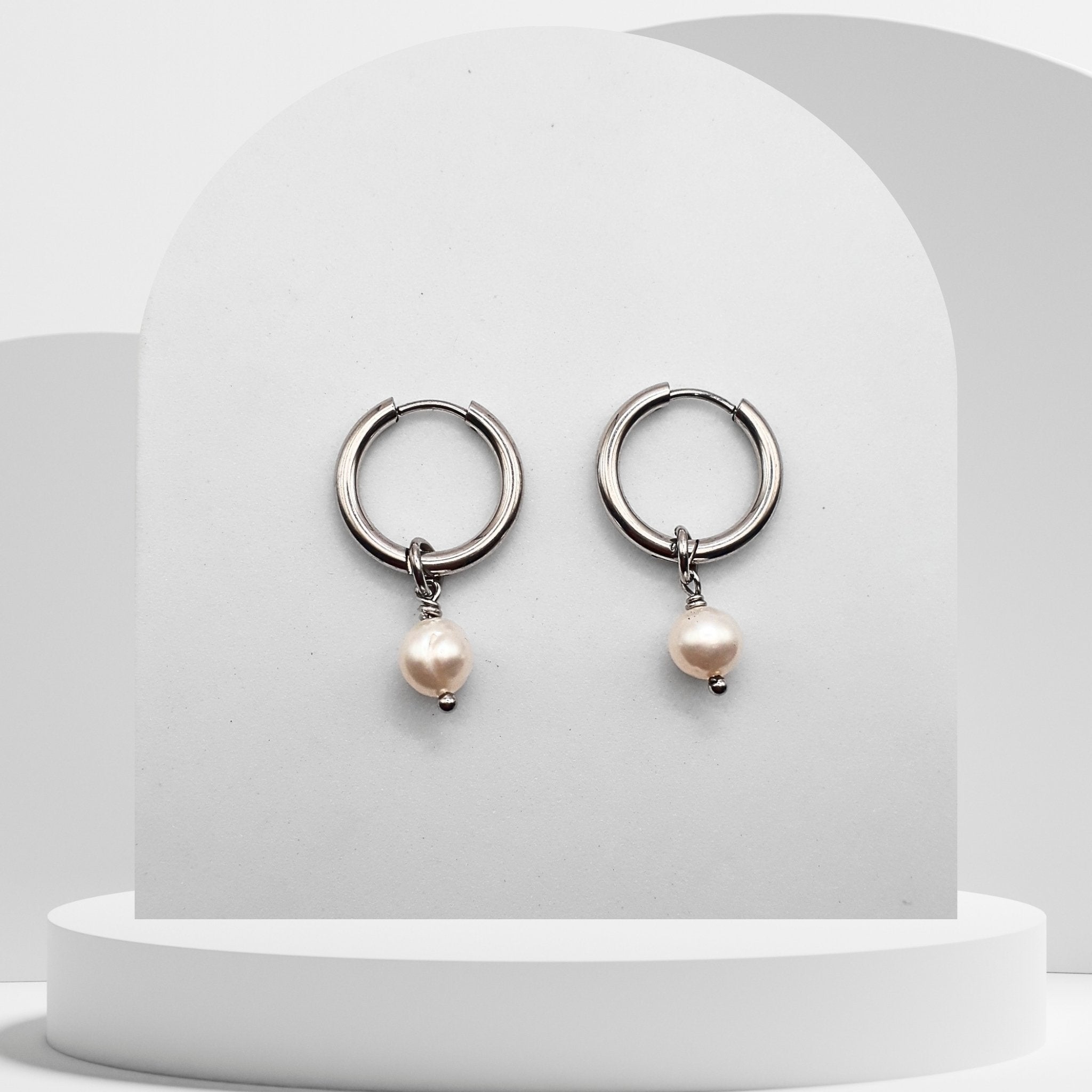 Silver hoop earrings with pearl drops on a white pedestal