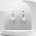 Pearl earrings on a white pedestal with a gray background