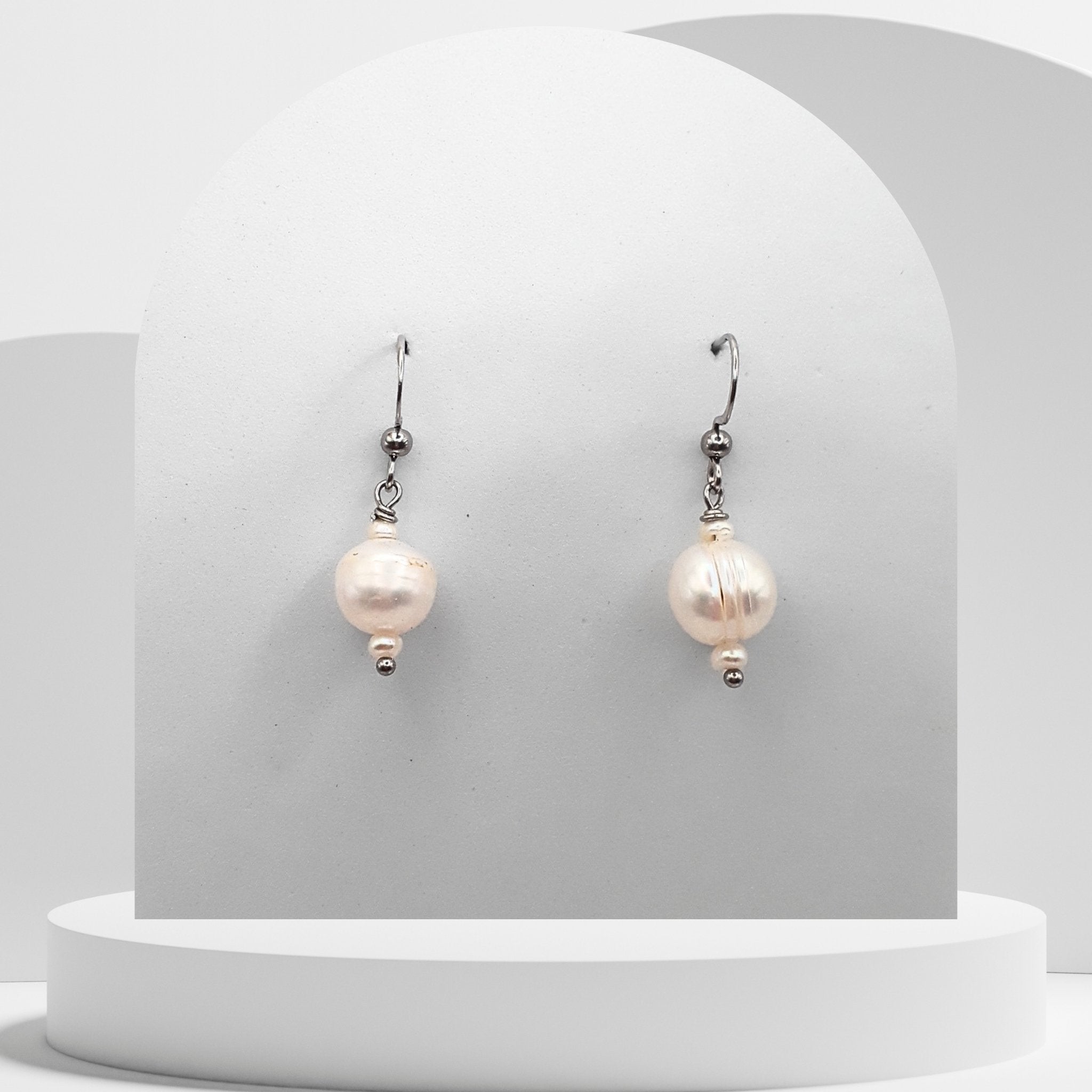 Pearl earrings on a white pedestal with a gray background
