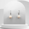 Pair of pearl earrings on a white pedestal with a gray background