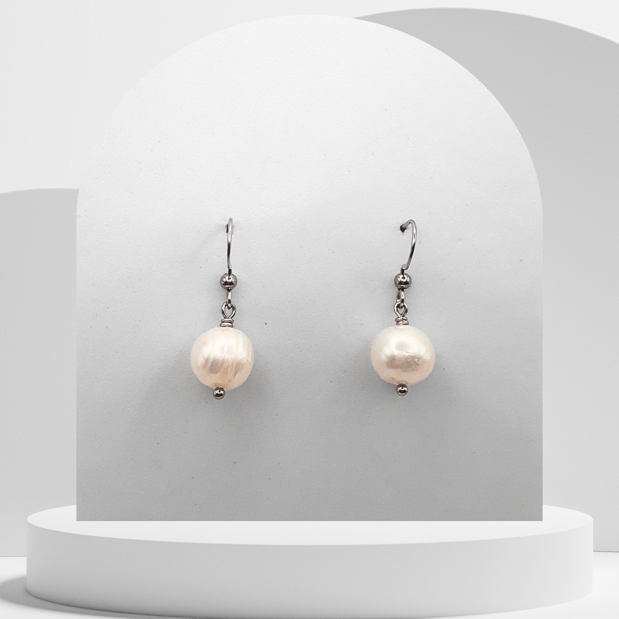 Pair of pearl earrings on a white pedestal with a gray background