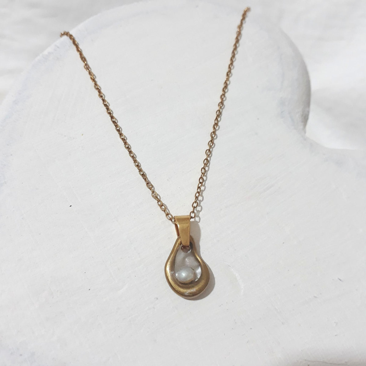This handmade necklace features a delicate white freshwater rice pearl within an organic open teardrop design, with a pearl-white background and a glass-like resin coating.