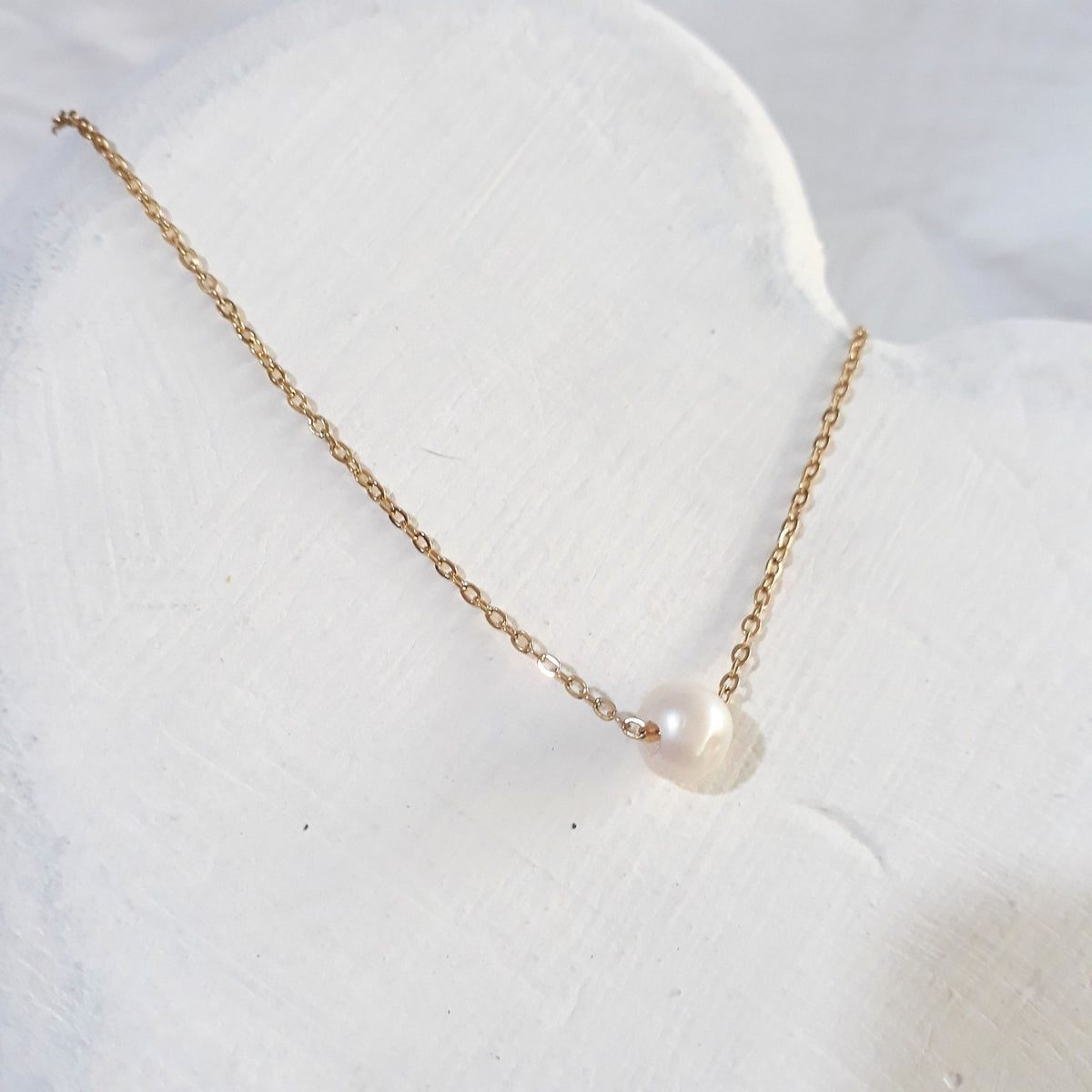 Gold plated floating single pearl necklace lying on a white wooden surface