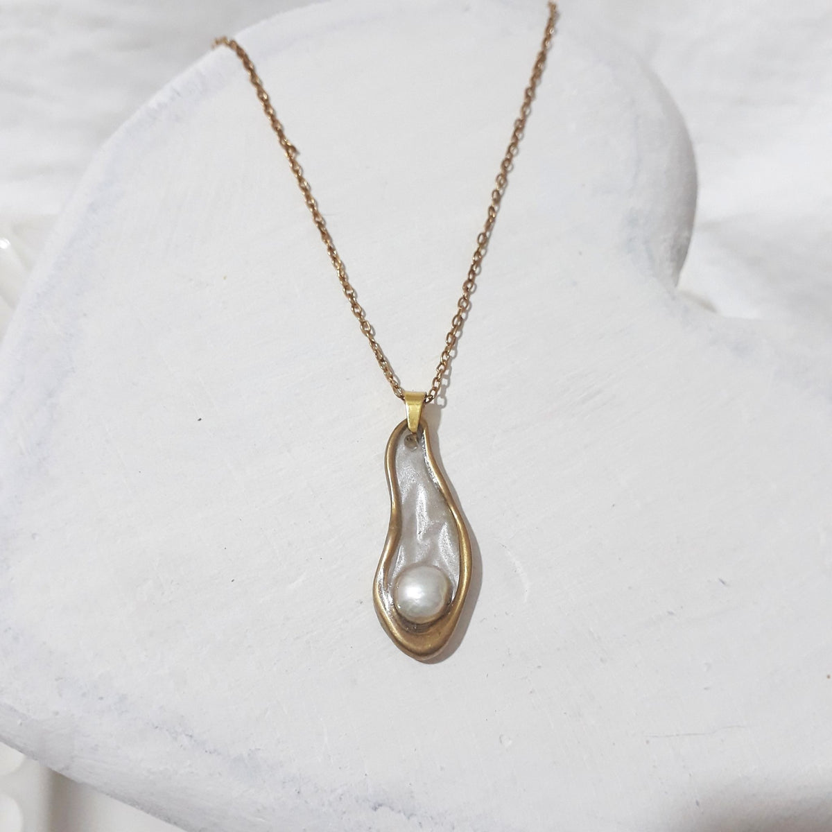This handmade necklace brings together a white freshwater pearl, an organic open teardrop pendant and a pearl-white background beneath a glass-like resin finish.