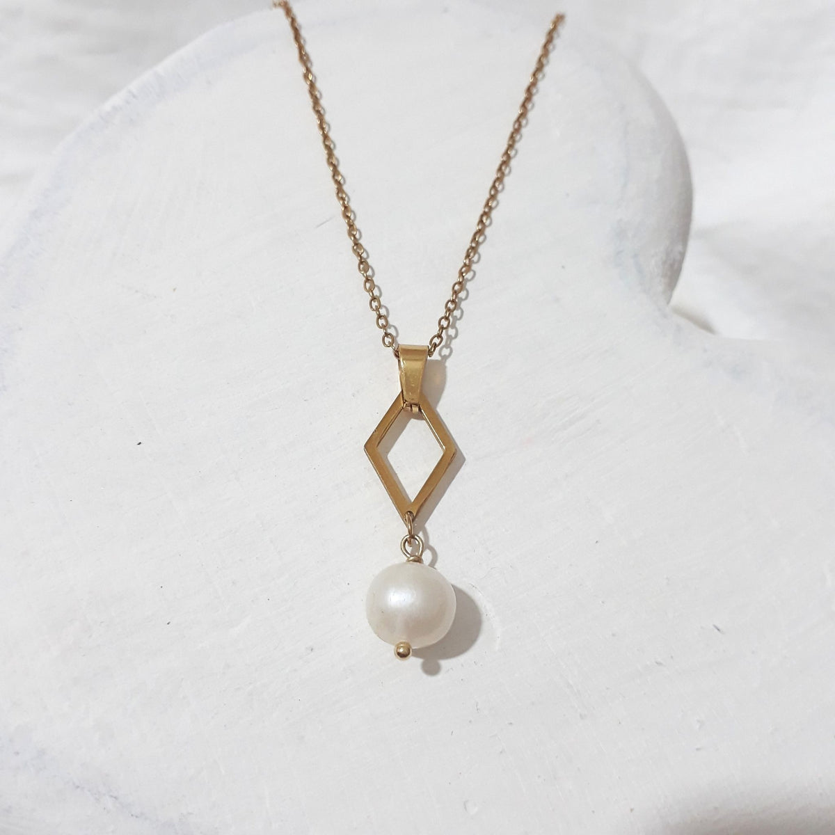 his handmade freshwater pearl necklace pairs soft white lustre with the clean lines of an open diamond-shaped pendant and the warm gleam of gold-plated stainless steel.