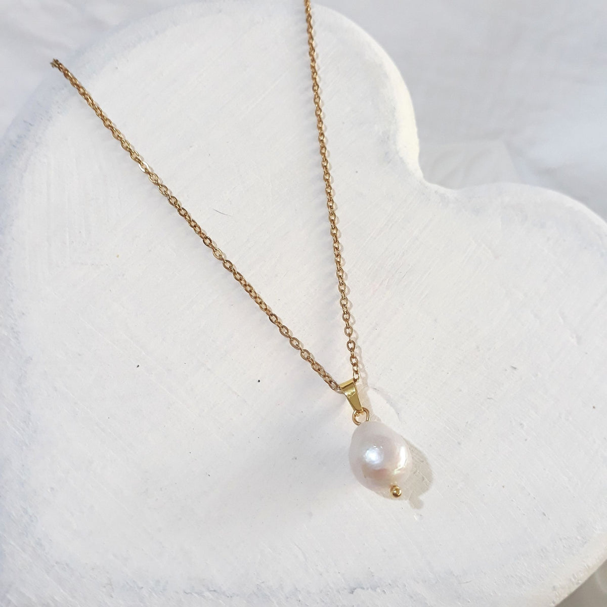 Gold-plated stainless steel 1mm white freshwater pearl necklace lying on a white wooden surface