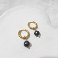 Small gold-tone hoop earrings with dark peacock freshwater pearl charms showing a blue-green sheen.