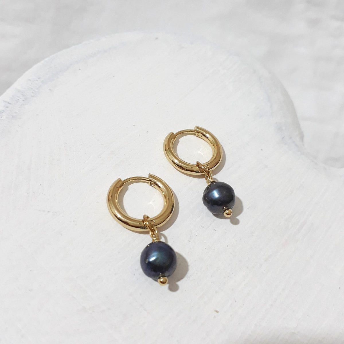 Small gold-tone hoop earrings with dark peacock freshwater pearl charms showing a blue-green sheen.