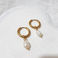 Small gold-tone hoop earrings with pear-shaped white freshwater pearl charms hanging beneath each hoop.
