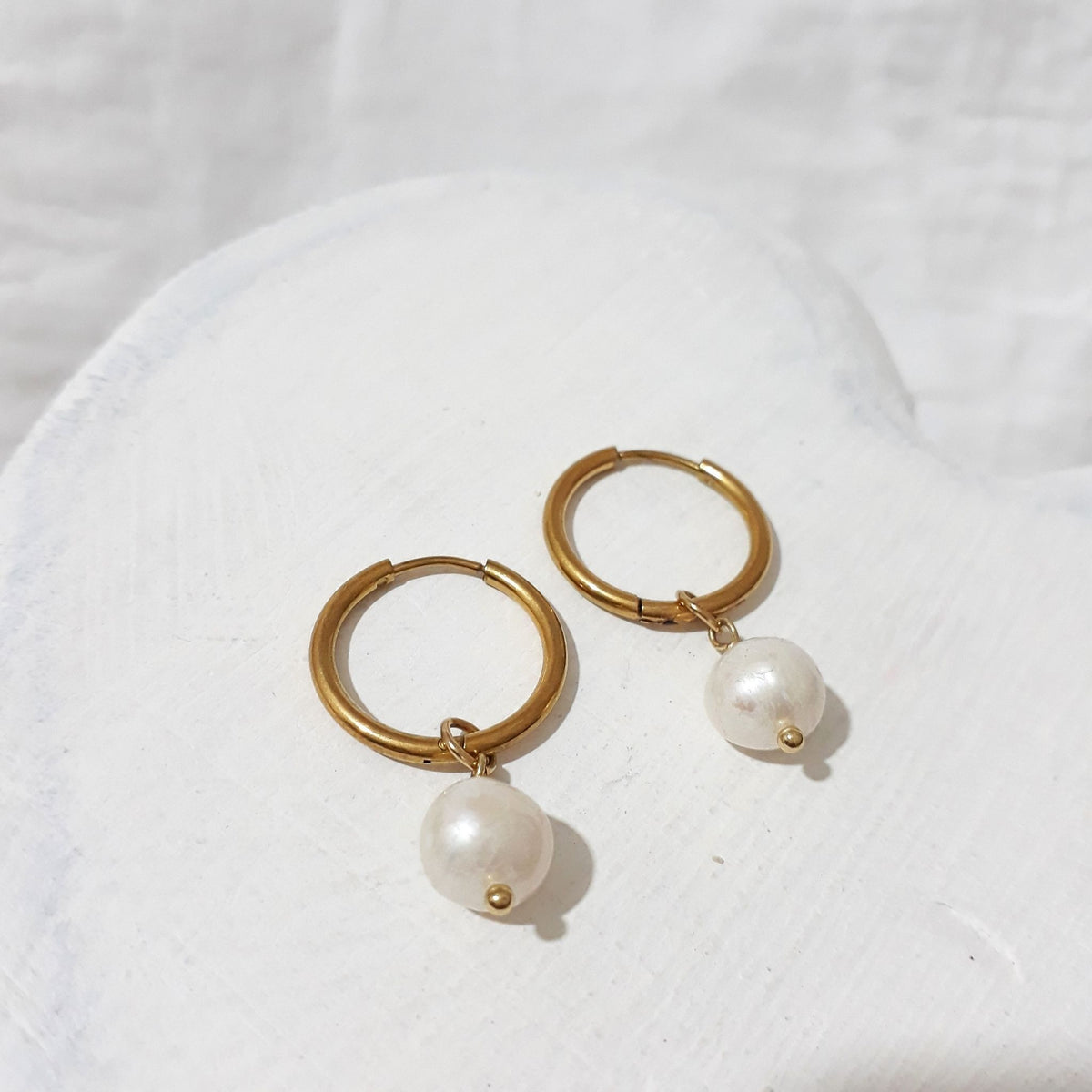 Gold-tone hoop earrings with near-round white freshwater pearl charms suspended beneath each hoop.