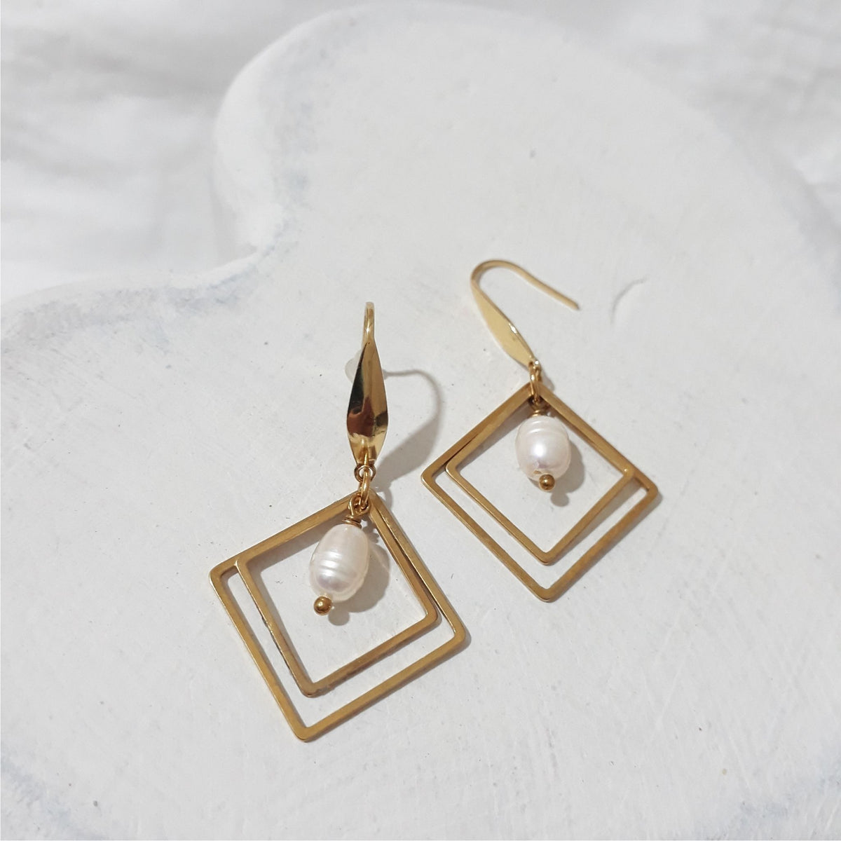 Gold-plated stainless steel earrings with nested diamond-shaped frames and an oval white freshwater pearl suspended inside each, on elegant hooks.