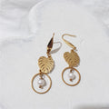 Gold-plated monstera leaf dangle earrings with round white freshwater pearls suspended inside open circles beneath the leaves.