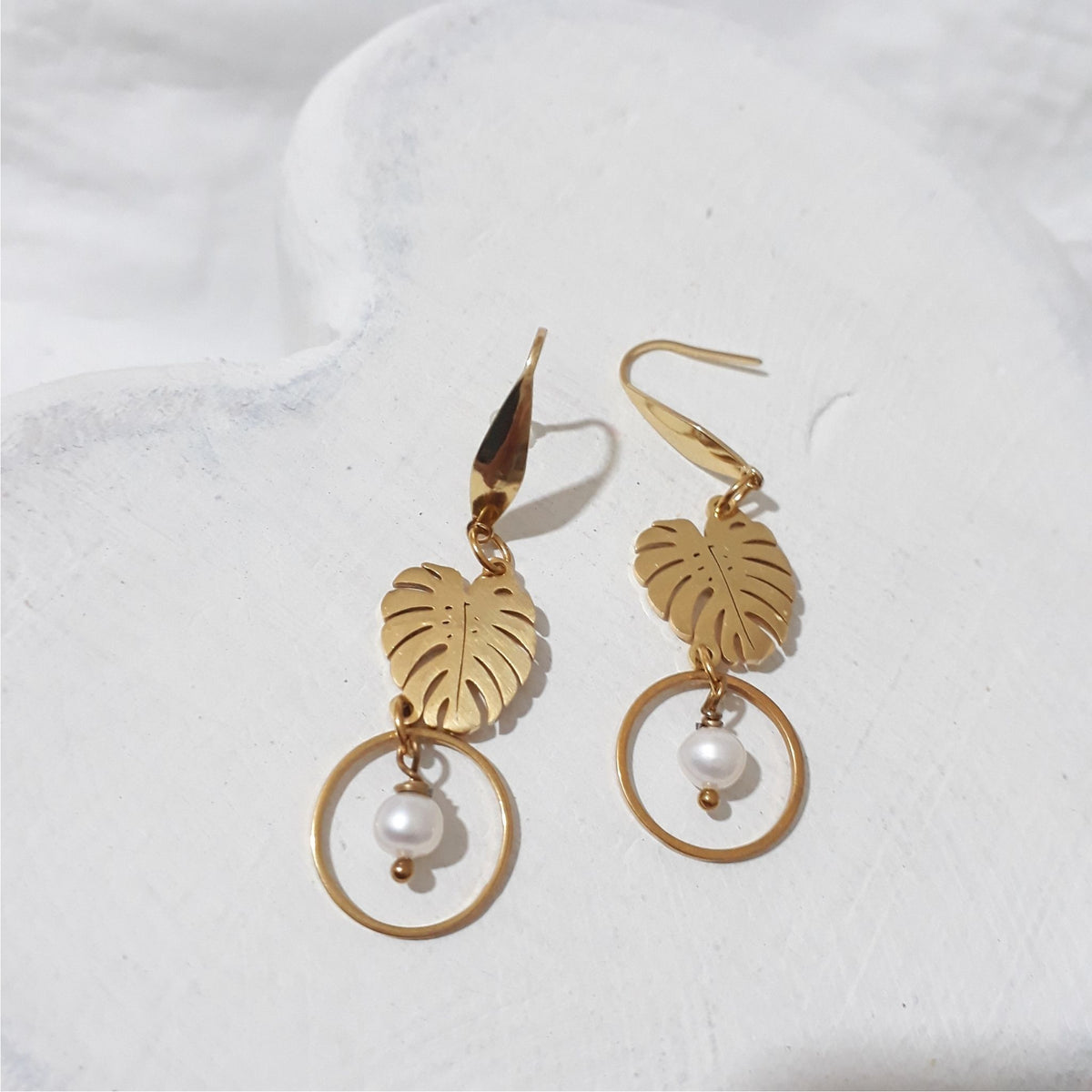 Gold-plated monstera leaf dangle earrings with round white freshwater pearls suspended inside open circles beneath the leaves.