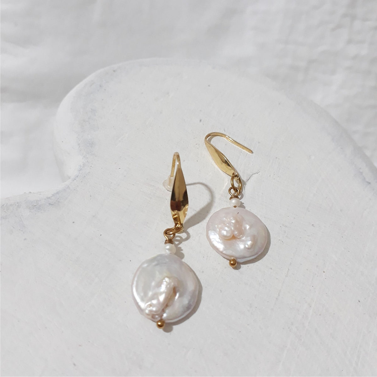 White freshwater coin pearl earrings with small white rice pearls above the coin pearls and gold-plated elegant ear hooks.