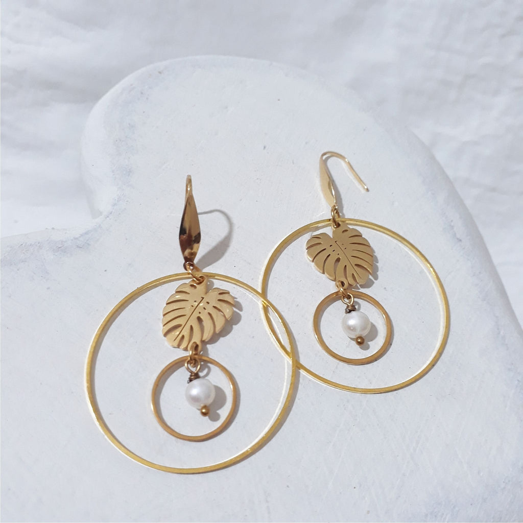 Gold-plated open hoop earrings with monstera leaf charms suspending smaller circles and round white freshwater pearls.