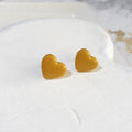 Glossy golden mustard-yellow heart-shaped polymer clay stud earrings with softly rounded edges.