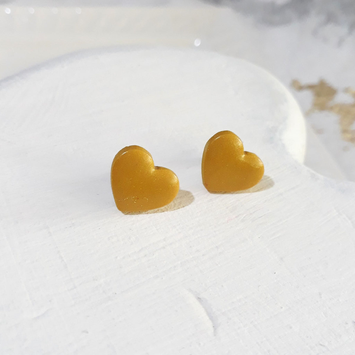 Glossy golden mustard-yellow heart-shaped polymer clay stud earrings with softly rounded edges.