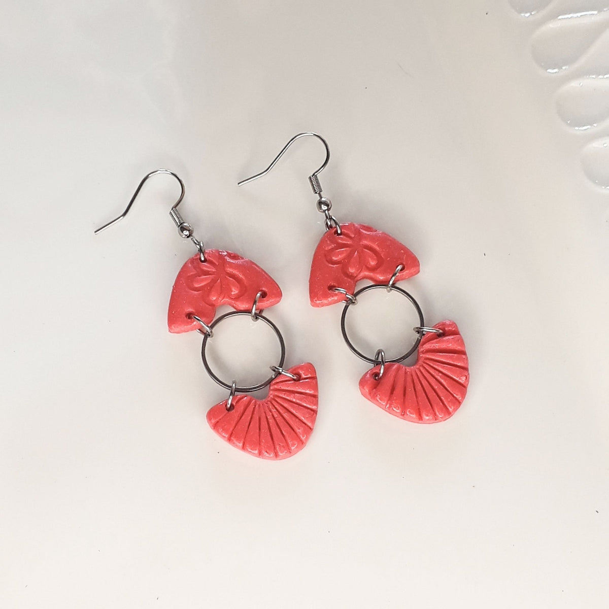 Handmade salmon pink textured fan and floral polymer clay dangle earrings on white display tray