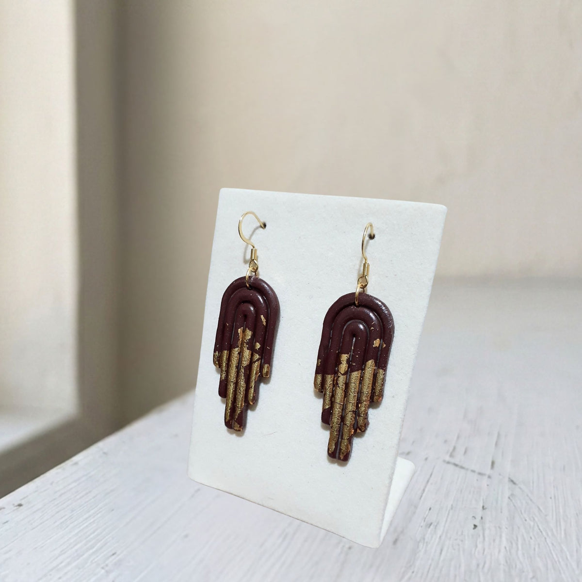 Handmade dark brown and gold arch polymer clay dangle earrings on white display stand