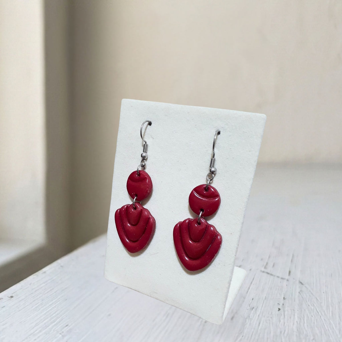 Handmade dark maroon layered teardrop polymer clay dangle earrings on white display stand