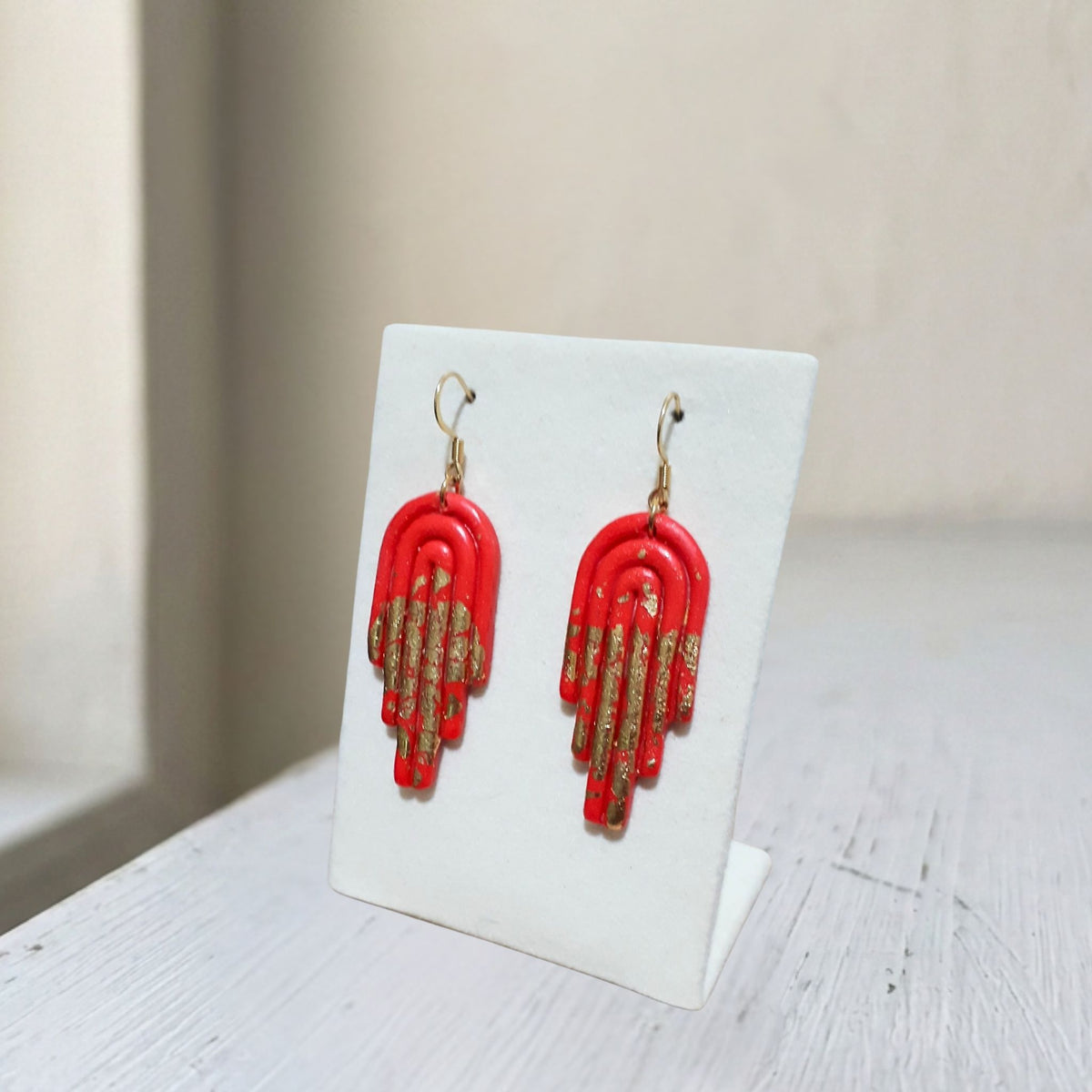 Handmade red and gold arch polymer clay dangle earrings on white display stand