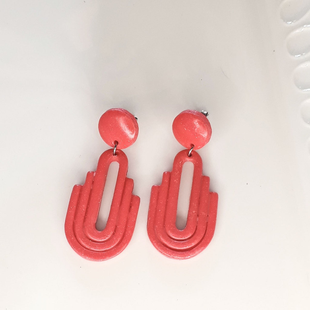 Handmade salmon pink Art Deco arch cutout polymer clay drop earrings on white display tray